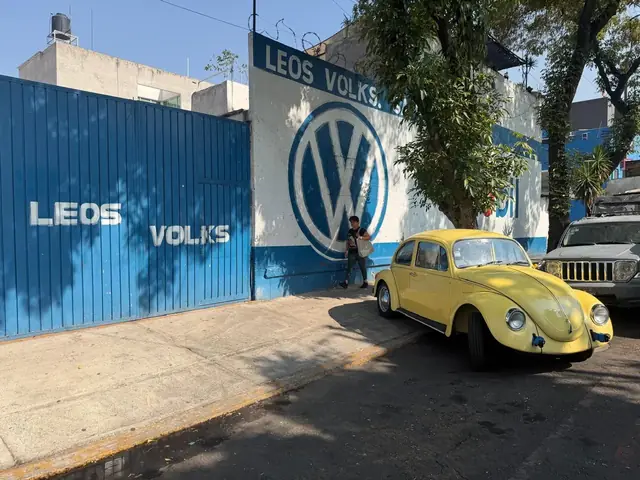 Vocho amarillo frente al mural del taller con el logo de Volkswagen