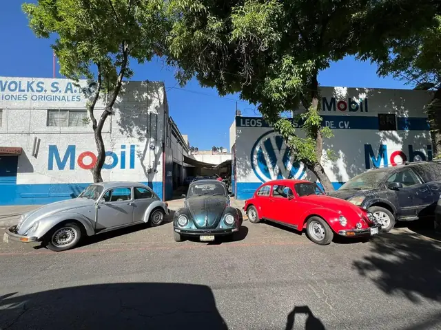 Tres vochos clásicos, plata, negro y rojo, estacionados frente al taller